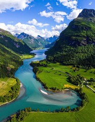 Aerial view of a turquoise river meandering through a lush green valley, nestled between majestic mountains under a vibrant blue sky