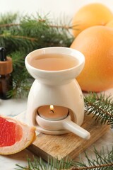 Aroma lamp with burning candle, grapefruits and fir tree branches on white table, closeup