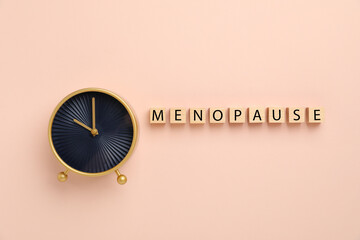 Wooden cubes with word Menopause and alarm clock on beige background, top view