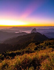 Vibrant sunrise paints a mountainous landscape with hazy valleys and golden foreground grasses, creating a serene, peaceful vista