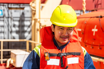 Merchant ship officer in blue overalls and yellow helmet, wearing lifejacket,  prepares lifeboat...