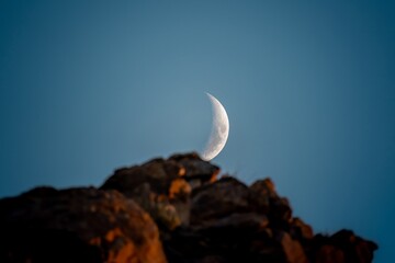 the moon is behind the mountain in the desert at sunset.