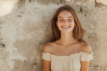Fototapeta premium Smiling young woman in off shoulder dress standing against rustic wall, cheerful lifestyle portrait in natural sunlight, candid expression showing happiness, confidence and positive mood 