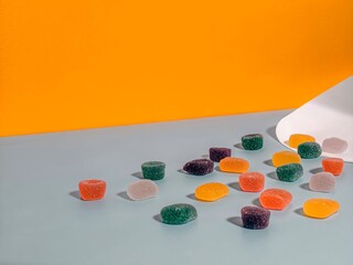 Colorful Gummy Candies Scattered on Light Blue Surface with Bright Orange Backdrop