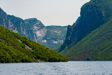 Fototapeta premium Western Brook Pond is a fjord located in Gros Morne National Park. The jagged mountains and rock wall are partially covered in lush green trees. The scenic area is accessible by ecotourism boat tours.