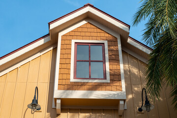 The exterior wall of a yellow wooden cottage. The Dutch gable roof has an extension on the top floor of the house. The eave is peaked with white and red trim. The siding is orange cedar shakes.
