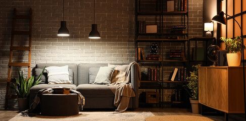 Interior of living room with bookshelf, sofa and glowing lamps at night