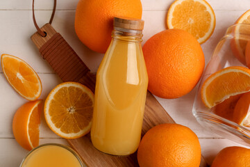 Oranges with glass bottle of tasty juice on white wooden background
