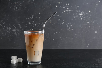 Glass of tasty iced coffee with straw and sugar cubes on black table