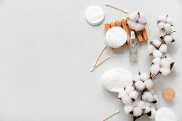 Composition with cosmetic products, beautiful cotton branch, pads and swabs on light background