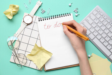 Female hand with to do list, wrist watch and stationery on turquoise background. Top view