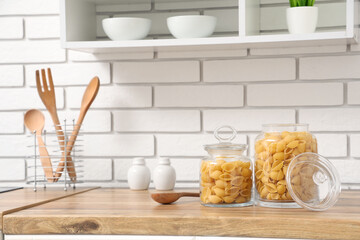 Jars with raw pasta shells on table near white brick wall in kitchen