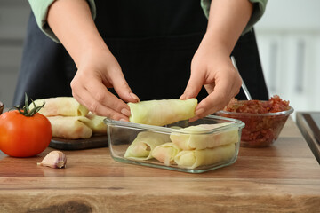 Woman preparing stuffed cabbage roll at table in kitchen, closeup
