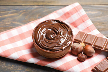 Bowl of sweet chocolate spread and hazelnuts on wooden background