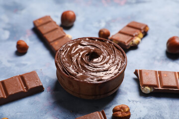 Bowl of tasty chocolate spread with hazelnuts on blue grunge background