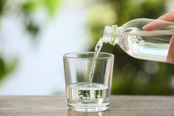 Woman pouring fresh water from bottle into glass outdoors, closeup