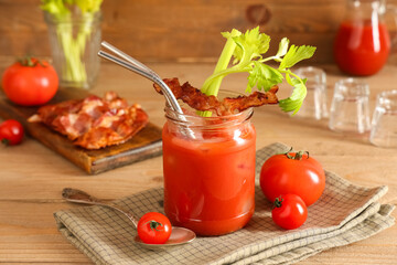 Mason jar of bloody mary cocktail with bacon and celery on wooden background