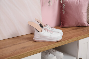 Sneakers with orthopedic insoles on bench near pink wall in hallway, closeup