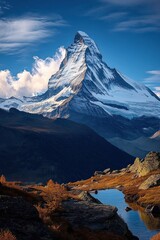 Majestic snow-covered mountain peak towering above autumnal forest and reflecting calm blue sky in a clear tranquil mountain lake