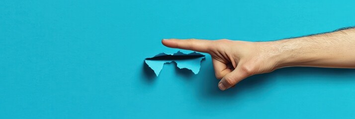 A human hand and forearm pressing down on a blue paper surface, causing a torn hole that reveals a darker blue layer beneath, conveying curiosity and exploration