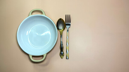 Empty ceramic bowl with spoon and fork on beige background