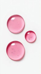 Close-up of translucent pink liquid droplets with bubbles, captured against a clean white background.