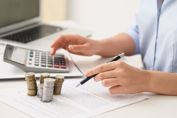Businesswoman with coins using calculator at table in office, closeup. Tax concept