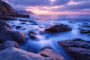 peaceful rocky coastline at twilight with soft waves flowing over large stones under a dramatic cloudy sky