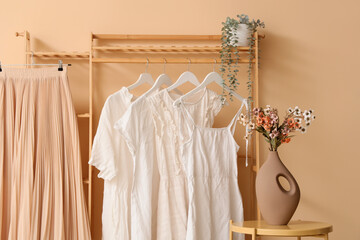 Rack with stylish clothes near beige wall in store