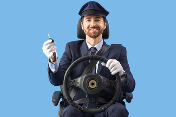 Handsome chauffeur with steering wheel and key sitting in car seat against blue background