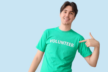 Male volunteer pointing at his t-shirt on light background