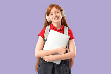 Fototapeta premium Cute schoolgirl with modern laptop and headphones on lilac background
