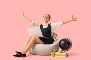 Female student with laptop studying computer sciences on beanbag against pink background