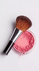 A makeup brush rests elegantly on a compact of vibrant pink blush powder against a minimalist white background.