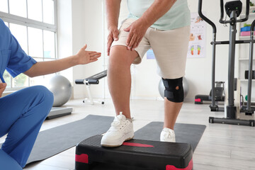 Senior man exercising on stepper with therapist in rehabilitation center