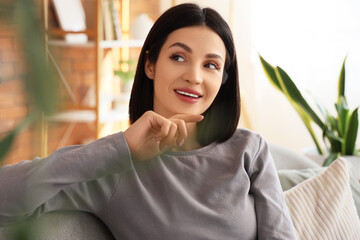 Fototapeta premium Thoughtful young woman sitting on sofa at home, closeup