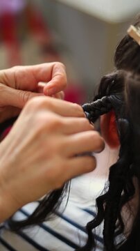 Vertical 4K video. Process of braiding African braids. White brunette woman in hair salon. Professional hairdresser is doing hairstyle. Female hand close up. Concept of beauty industry, job, work