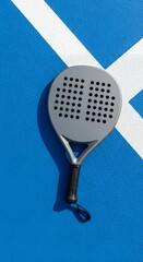 A grey paddle rests on a textured blue surface with white diagonal lines suggesting a sports court setting highlighting equipment Tennis Racquet Game Play Activity Outdoor Recreation