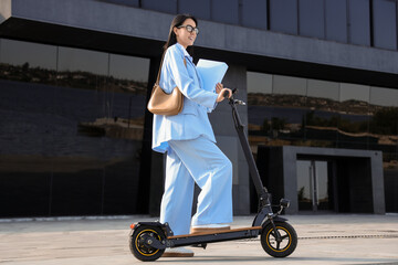 Young businesswoman with folders and electric scooter in city