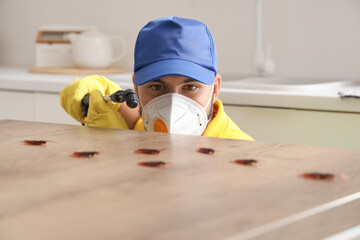 Male pest control specialist disinfecting table for cockroaches in kitchen, closeup