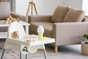 Baby highchair with bottle of milk and toys in living room