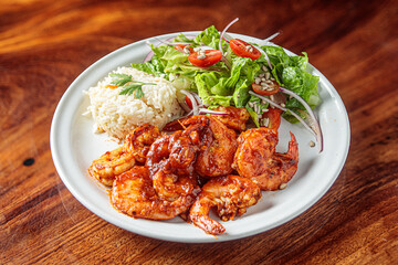 A plate of camarones a la diabla, spicy shrimp cooked in a rich red sauce, served with white rice and a side salad.