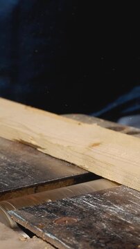 A man's hand runs a wooden plank through a woodworking machine that grinds and smooths the surface. Home woodworking workshop, wood processing.