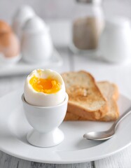 Soft-boiled egg in an egg cup, beside toast and a spoon
