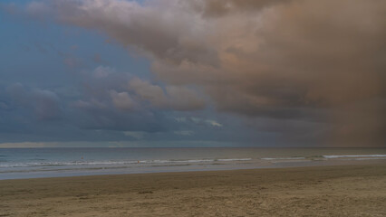 A quiet evening by the ocean. The waves are foaming and spreading across the sandy beach. The clouds in the blue sky are highlighted in pink and gold. Malaysia. Borneo. Kota Kinabalu.