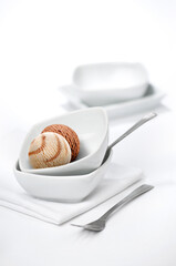 A scoop of ice cream served in a white bowl. A casually placed white bowls on a white background with chocolate ice cream. Beautiful and uncluttered dessert food photography.