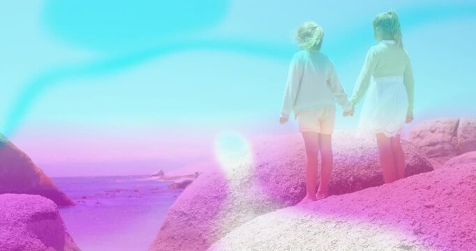 Sisters standing on rock, left sister lifting arm pointing at view with pastel flares for travel