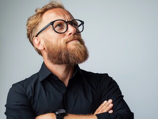 Thoughtful man with glasses and beard looking up against a plain background in a studio setting for creative concepts