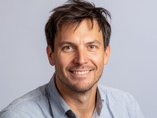 Smiling man with short dark hair wearing a blue shirt against a light background capturing a genuine friendly expression