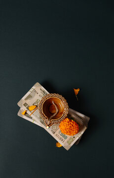 Money is worshiped as a Goddess Laxmi during Diwali festival. A symbolic custom to perform Lakshmi puja with currency notes. Indian rupee notes with flower and Diwali lamp from above.